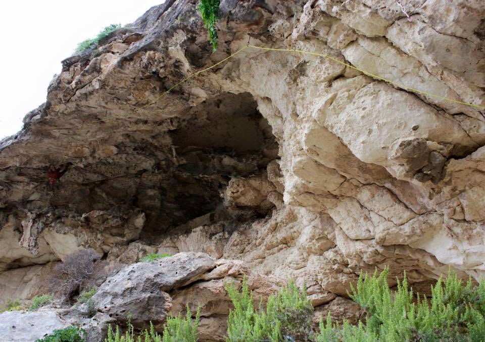 Għar tal-ġebla tal-franka u rdum sporġut b'ħabel jaqsam minn fuqu, arbuxxelli selvaġġi taħt