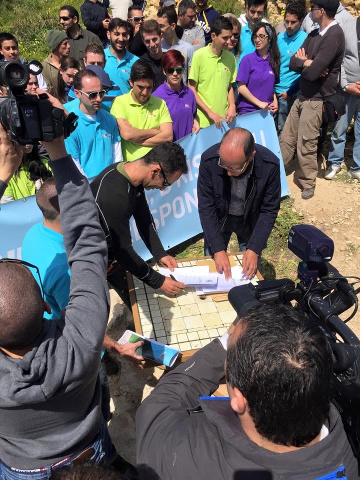 Żewġt irġiel jiffirmaw dokumenti fuq mejda barra, imdawra b'folla u kameras tal-aħbarijiet